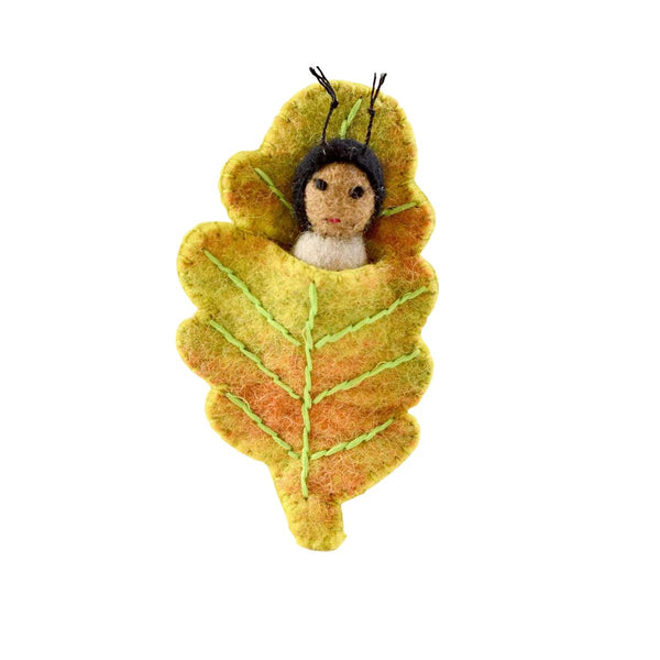 Felted caterpillar-like figurine nesting in a felt oak tree leaf on a white background