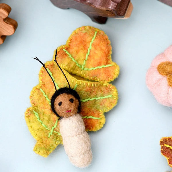 Felt toy figurine resting on an autumn-colour oak felt leaf on a light blue background