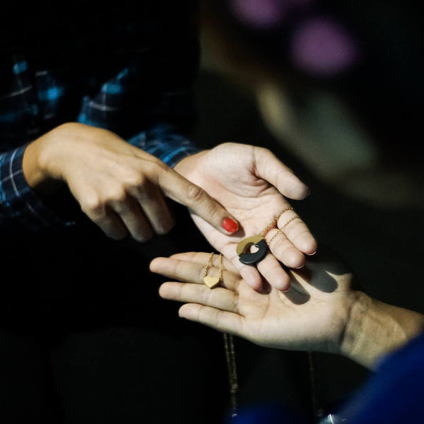 Hands exchanging a Committed necklace and a gold centre heart.